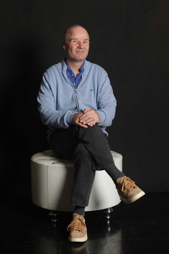 David-Roethle-Portrait - sitzend vor schwarzem Hintergrund auf weißem Hocker