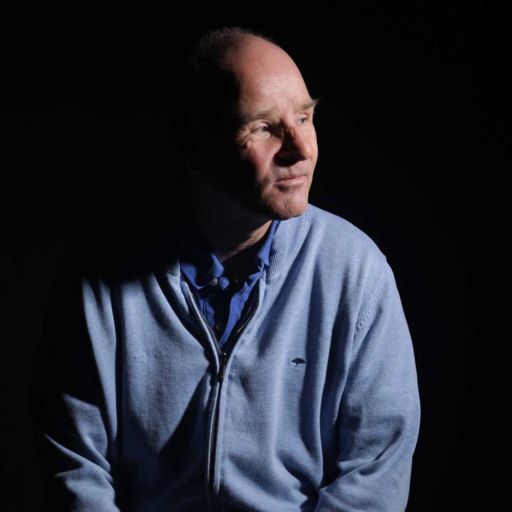 David Röthle nach links schauend und sitzend vor schwarzem Hintergrund.